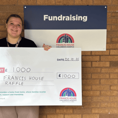 Woman holding a large cheque with the words £1000 pounds stood against a brick wall
