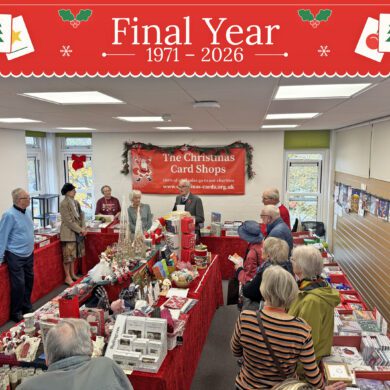 People stood in a room of tables covered in red tablecloths and christmas cards and gifts