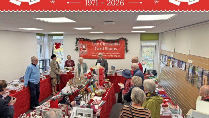 People stood in a room of tables covered in red tablecloths and christmas cards and gifts