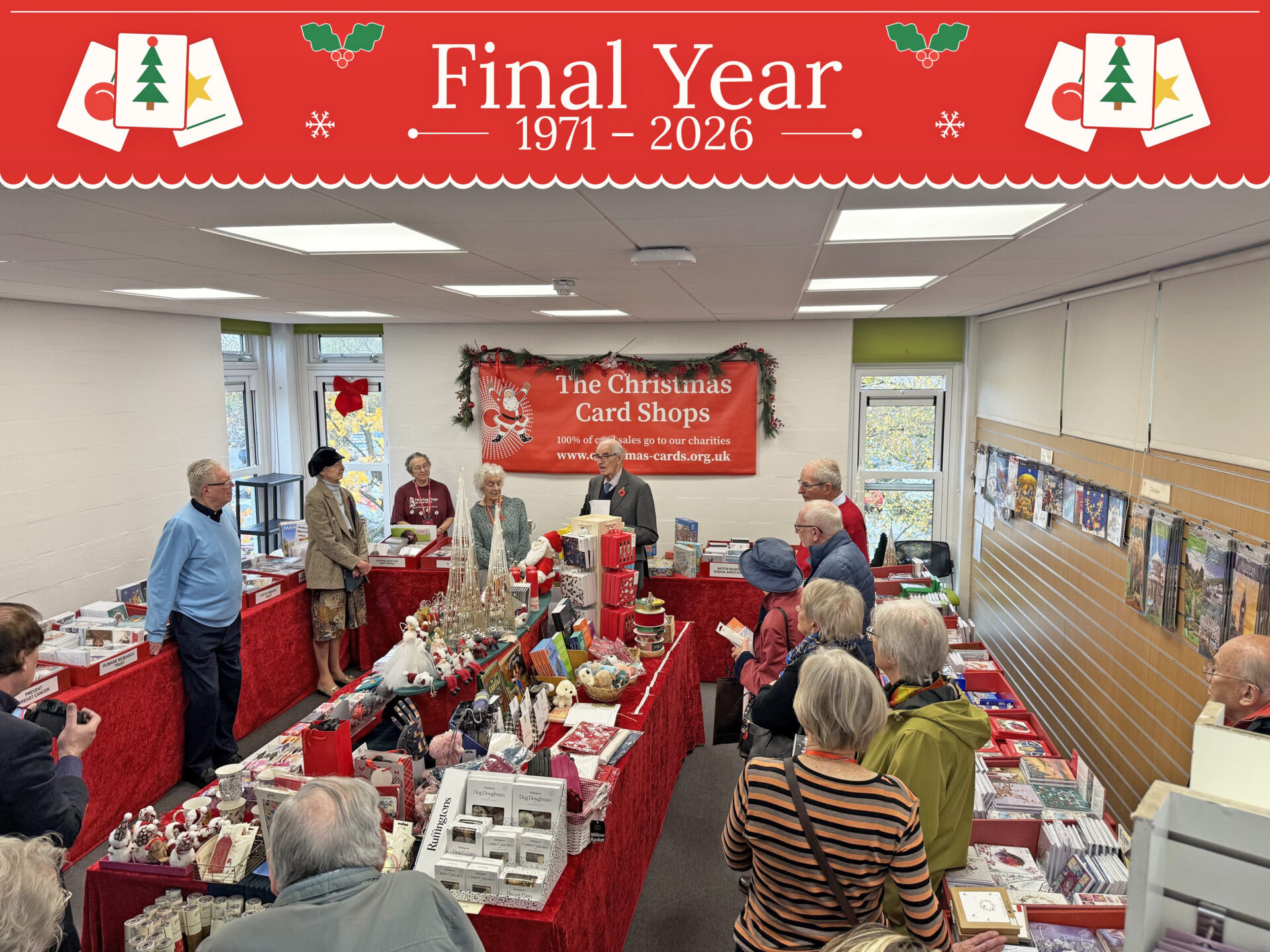 People stood in a room of tables covered in red tablecloths and christmas cards and gifts