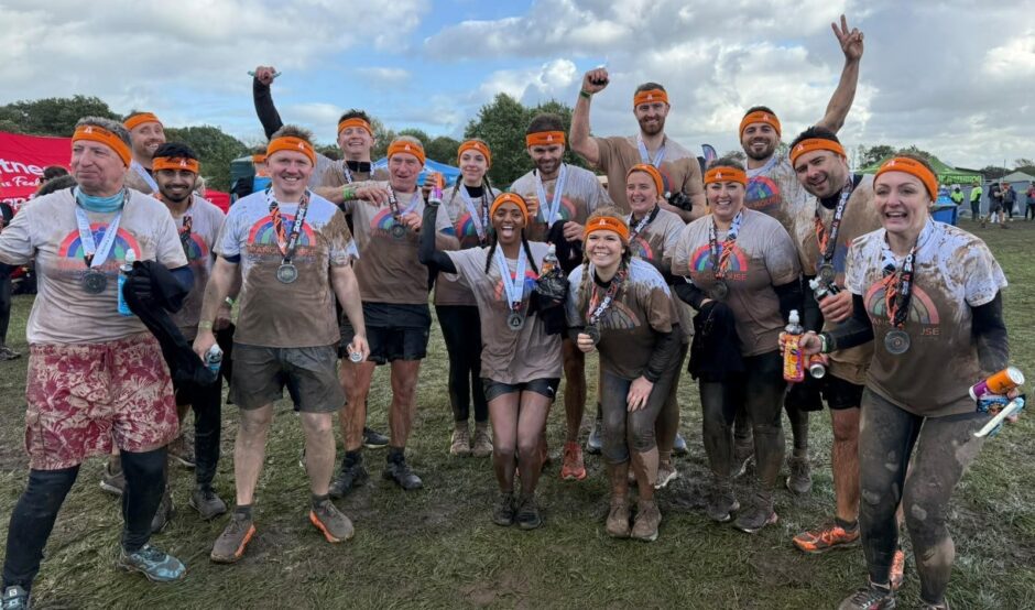 Large group of people wearing white t-shirts which are covered in mud holding medals after completing a Tough Mudder challenge event